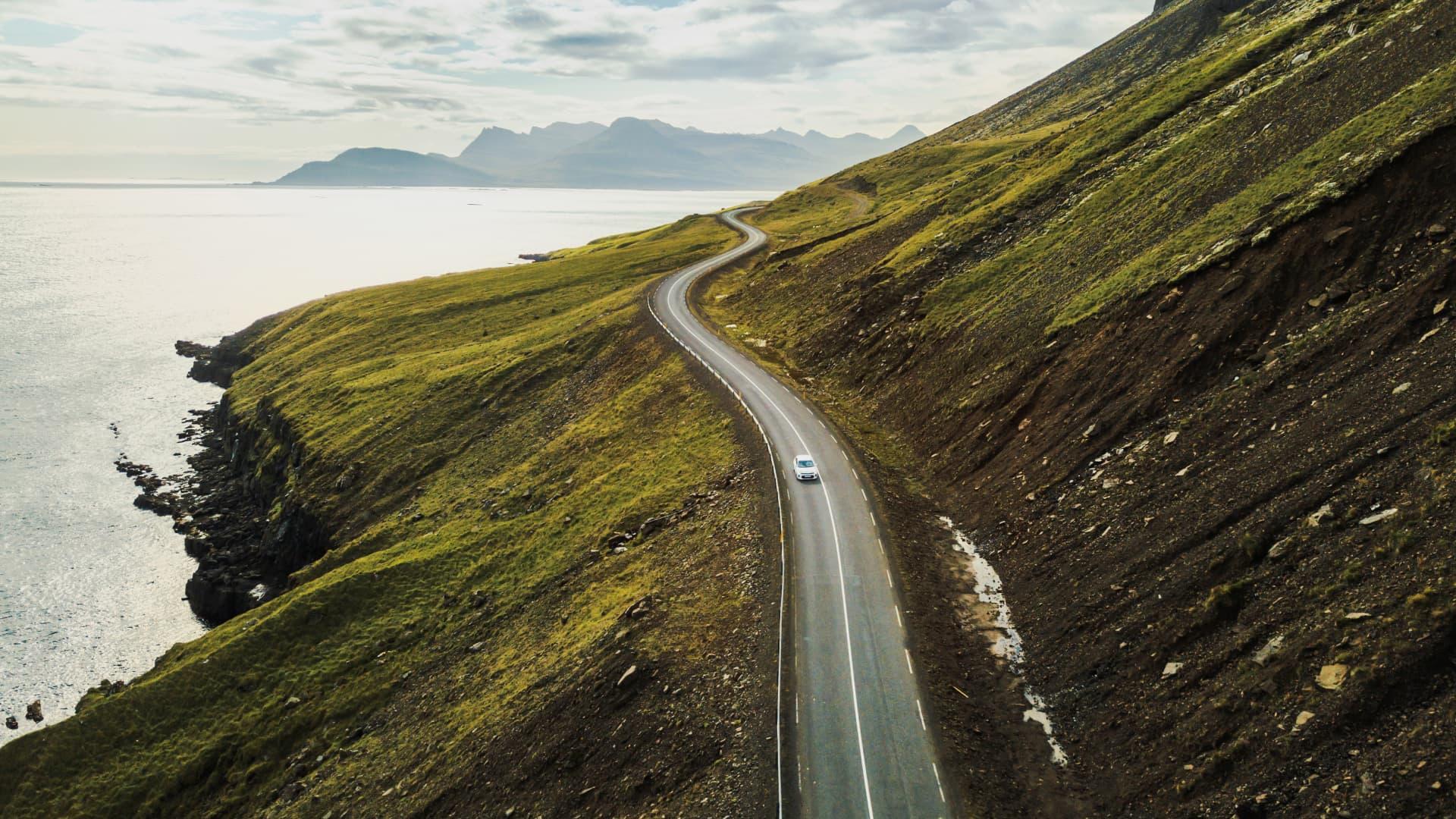 Winding road along a cliff with a single car and scenic ocean view in Iceland.
