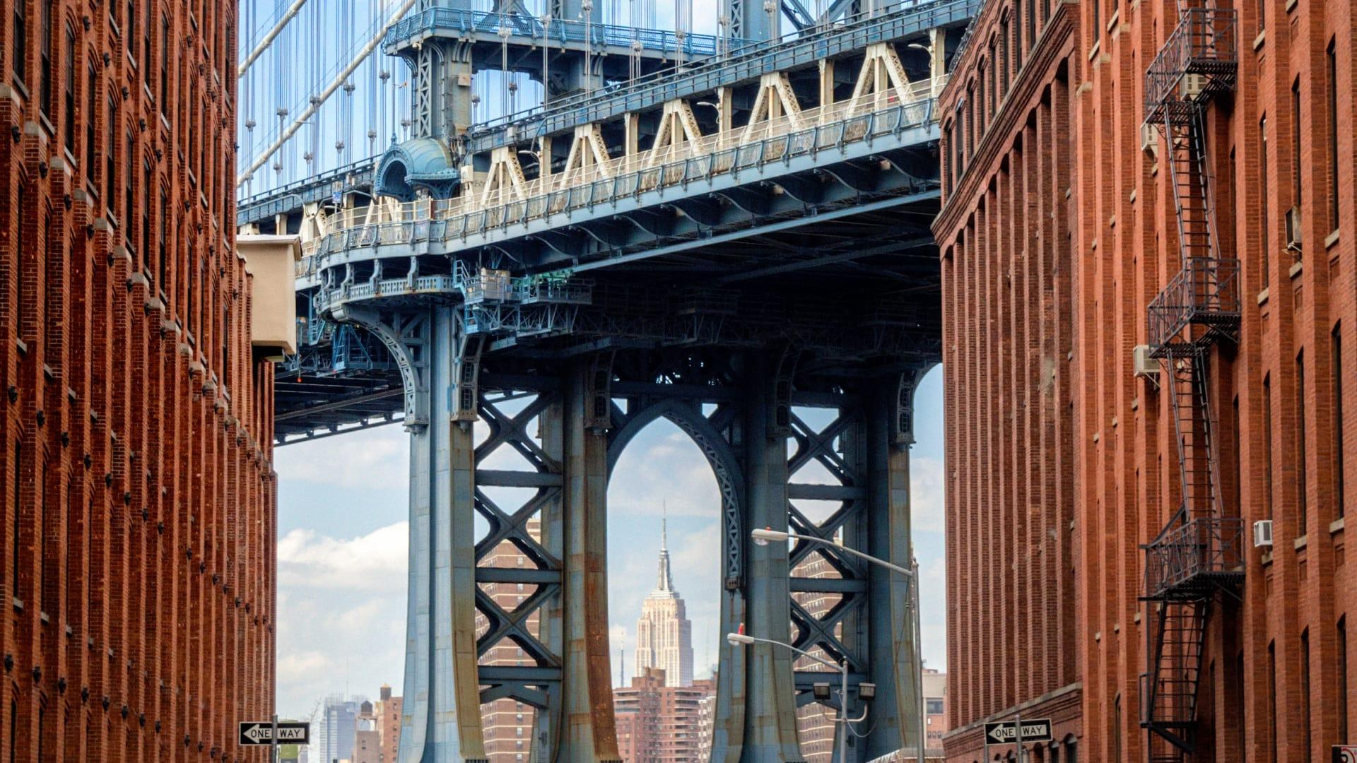 Manhattan Bridge framed between two brick buildings with Empire State Building in the background.