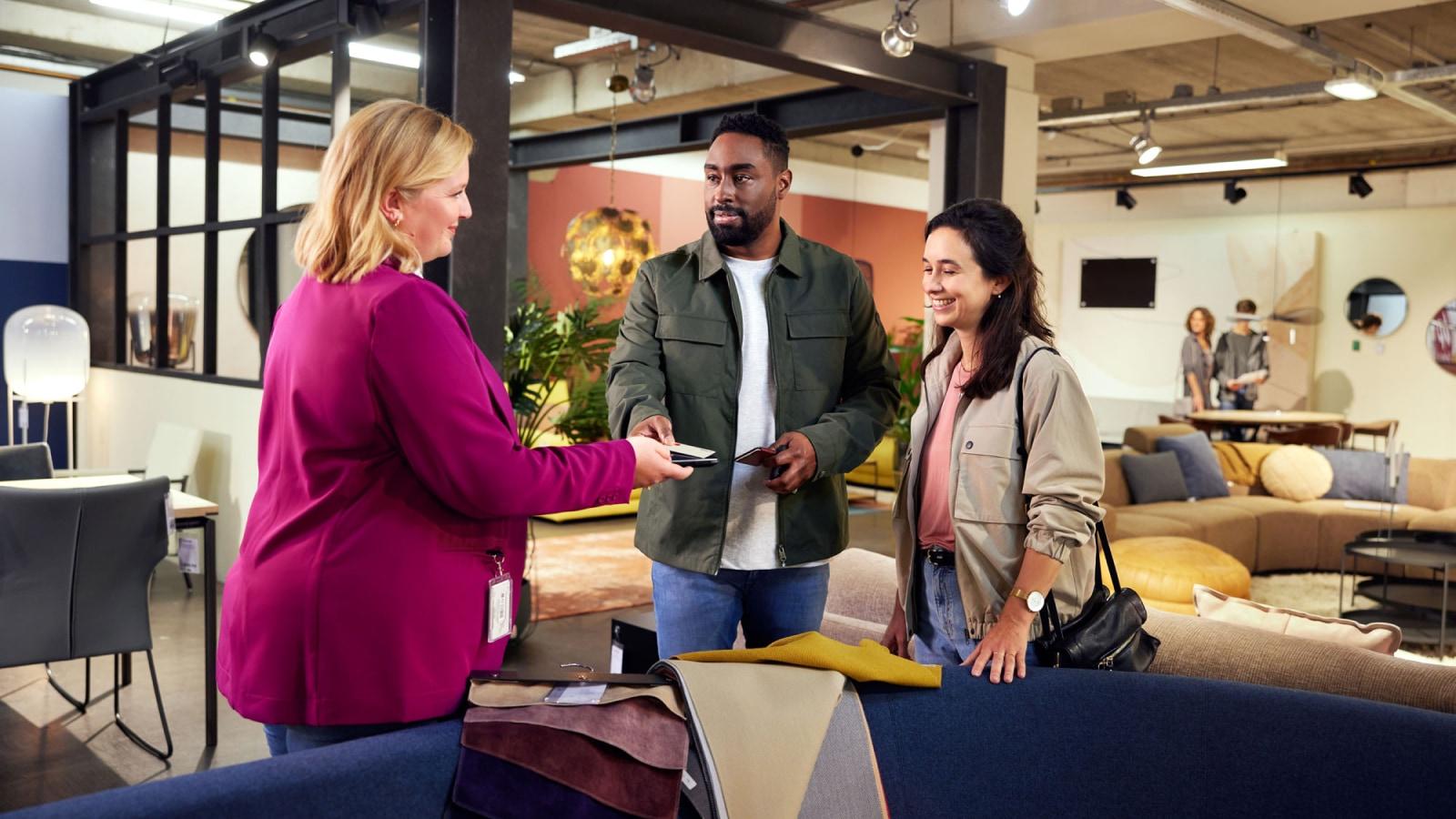 Two customers receiving a card payment device from a clerk in a modern store interior.