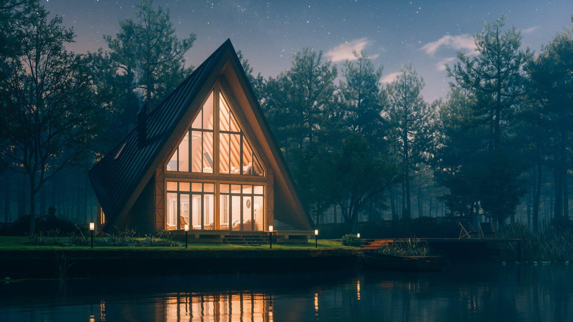 Maison en A avec fenêtres éclairées au bord d'un lac tranquille au crépuscule sous un ciel étoilé en Suède.