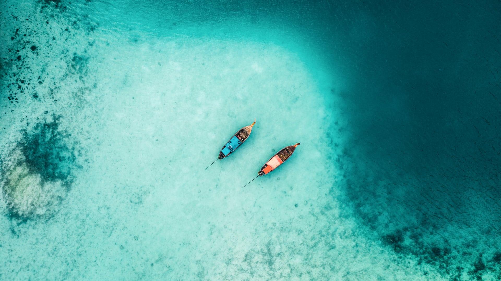 Aerial view of three colorful boats floating on clear blue waters in Thailand.