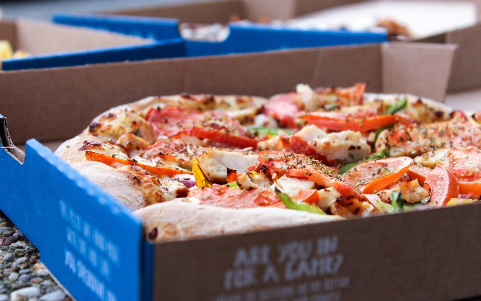 Visão close-up de uma pizza fresca com vários toppings em uma caixa de cartão.